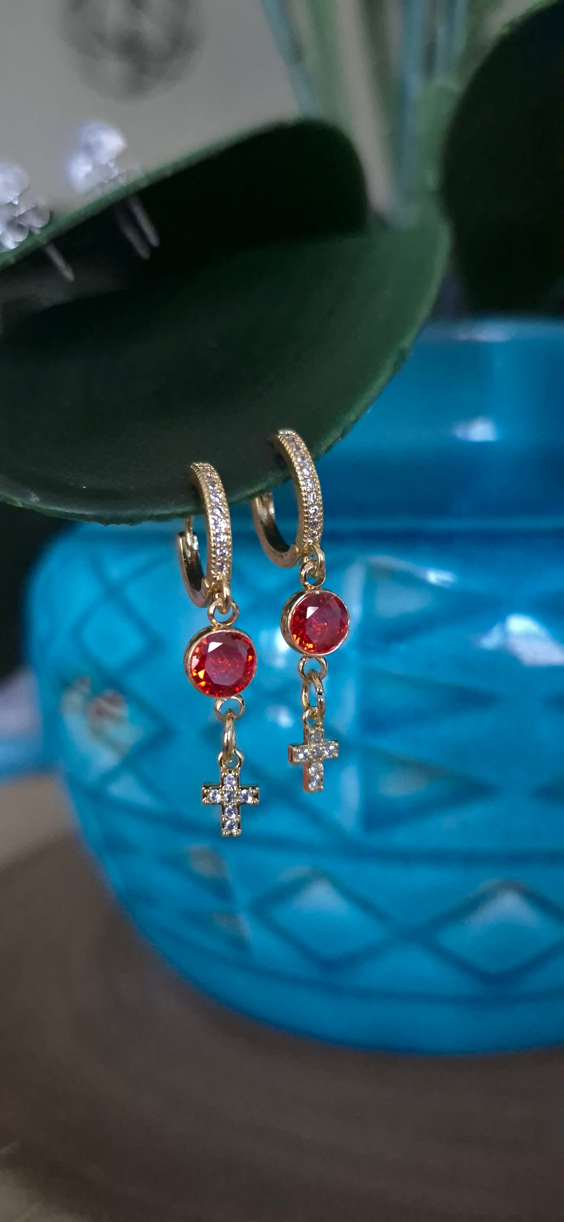 Gold-tone hoop earrings with red stones and dangling cross charms, front view