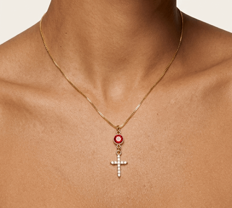 Gold cross necklace with red oval stone and white zircon details on pendant